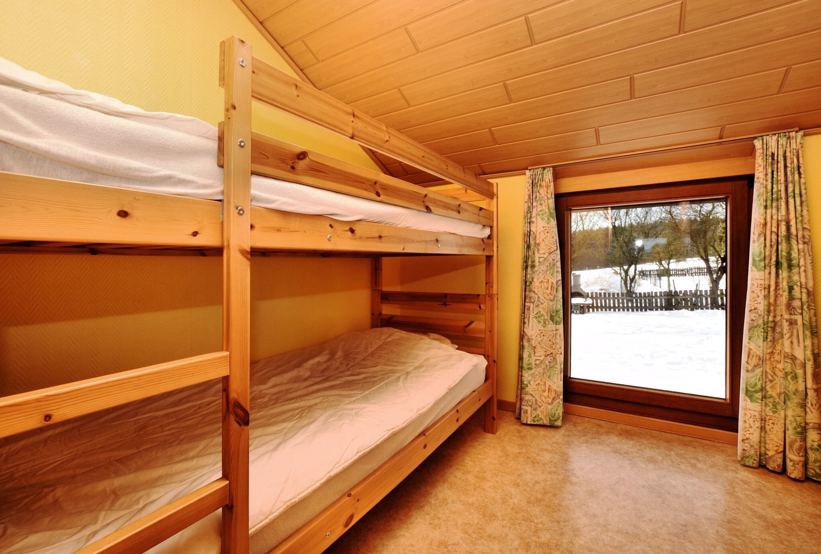 A bunk bed room with a wooden ceiling and a window with curtains.