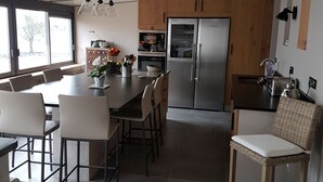 Moderni keittiö, jossa on ruokailutila, suuri keittiösaareke, ruostumattomasta teräksestä valmistetut kodinkoneet ja näkymä ikkunasta.