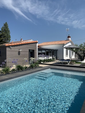 Una casa moderna con piscina, rodeada por un jardín de flores moradas y una zona de patio.