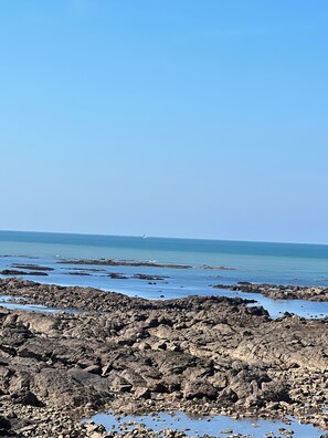 Una costa rocosa con agua azul cristalina y un velero a lo lejos.