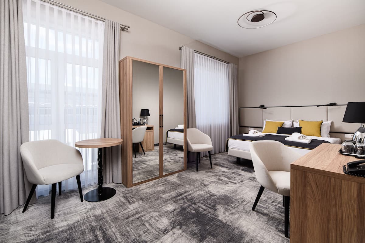 Quarto de hotel com uma cama, duas cadeiras, uma escrivaninha, um espelho e uma mesinha.