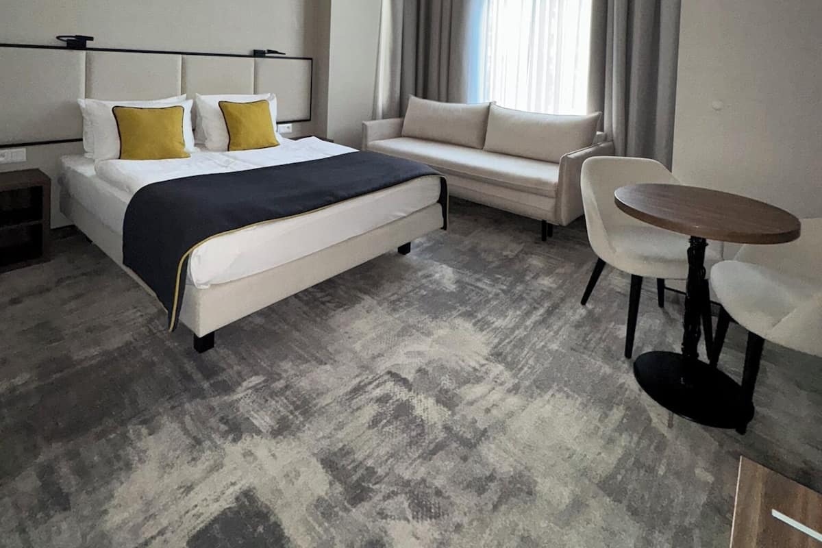 Quarto de hotel moderno com cama, sofá e pequena mesa de jantar.