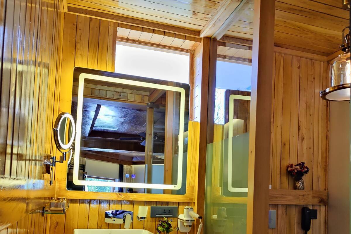 Baño de cabaña de madera con un espejo grande, lavamanos, inodoro y zona de ducha.