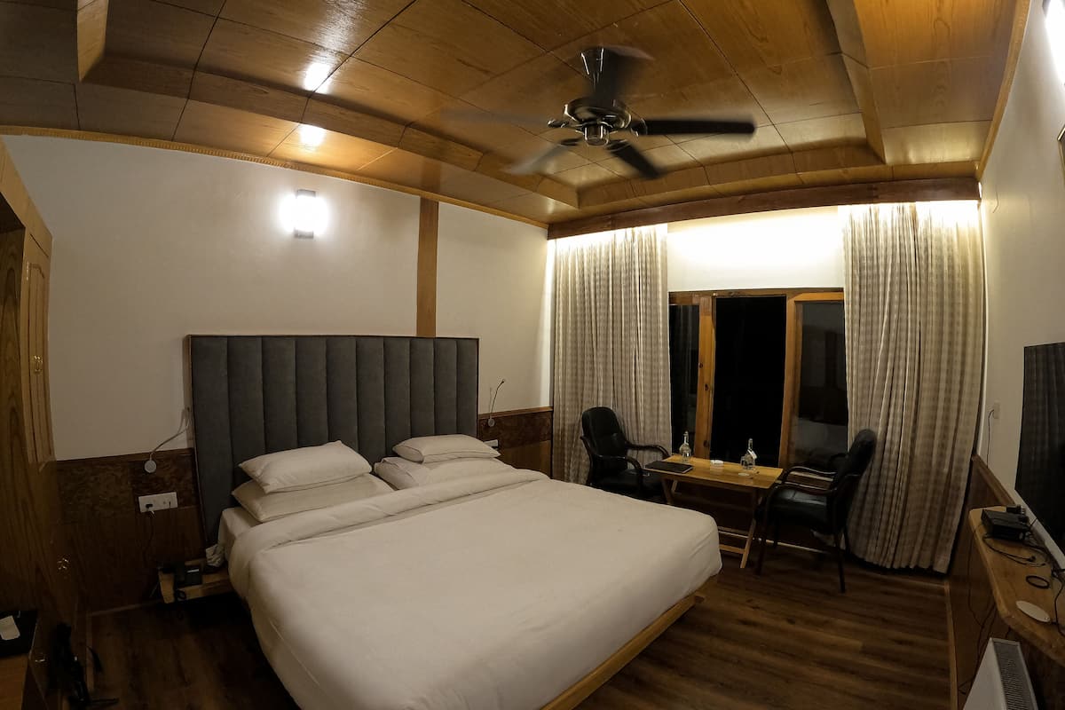 Una habitación de hotel con una cama grande, un escritorio con silla, un ventilador de techo y una ventana con cortinas.