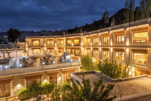 A multi-story hotel with a courtyard, outdoor seating, and a mountain backdrop. - Cho Palace (Leh)