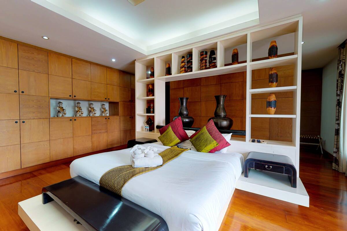 A modern hotel room with a large bed, wooden panel walls, and built-in shelves with decorative items.
