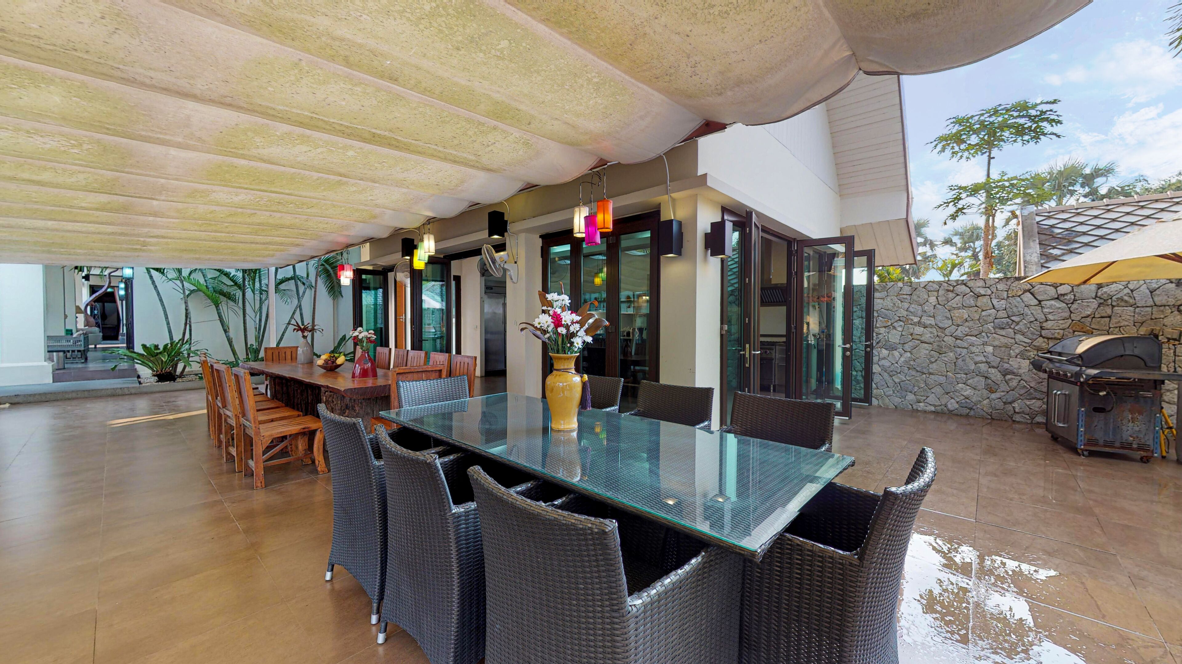 An outdoor dining area with a glass table, wicker chairs, and a stone wall.