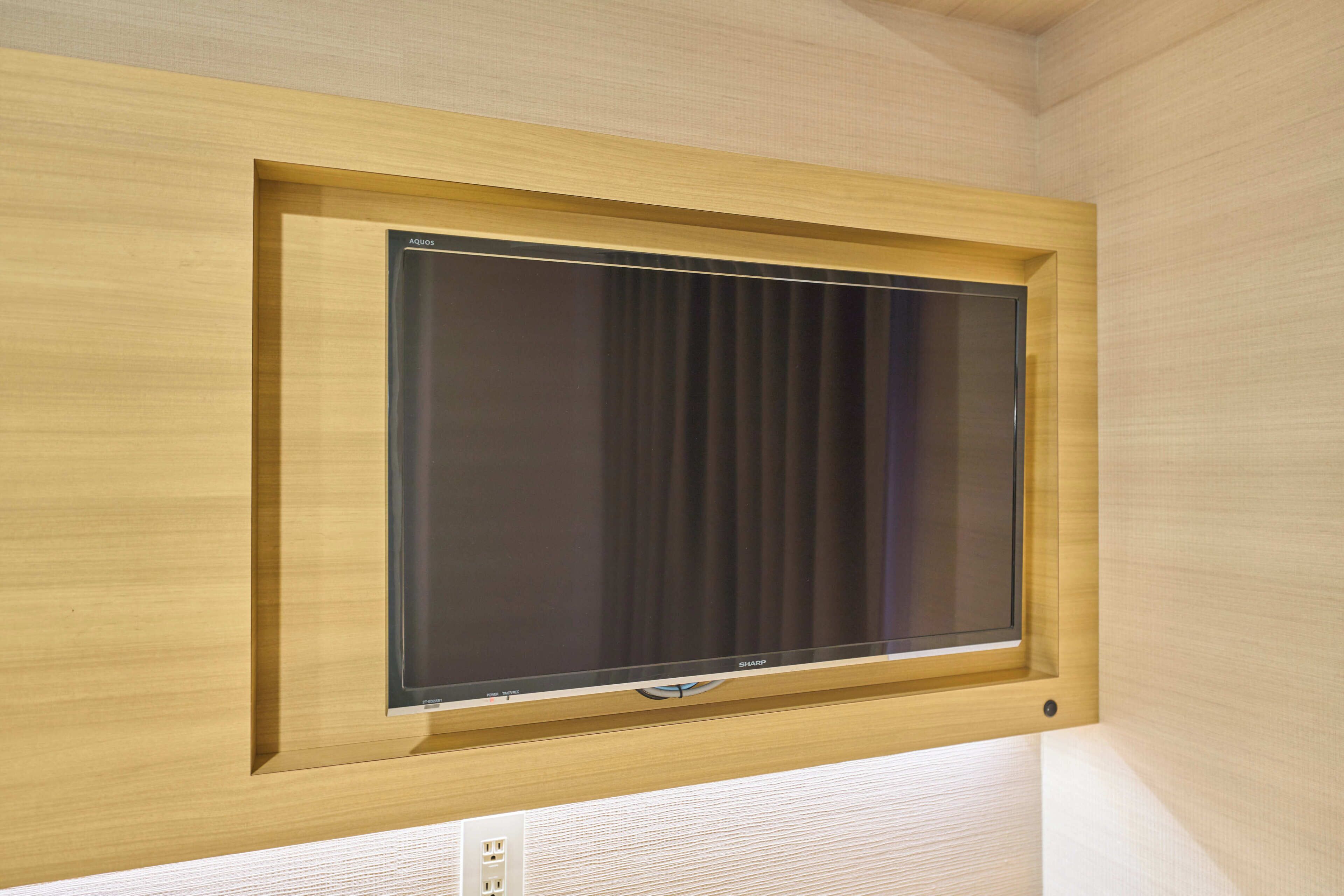 Habitación con un televisor de pantalla plana grande montado en una pared de madera, un enchufe debajo del televisor y una pared con textura.