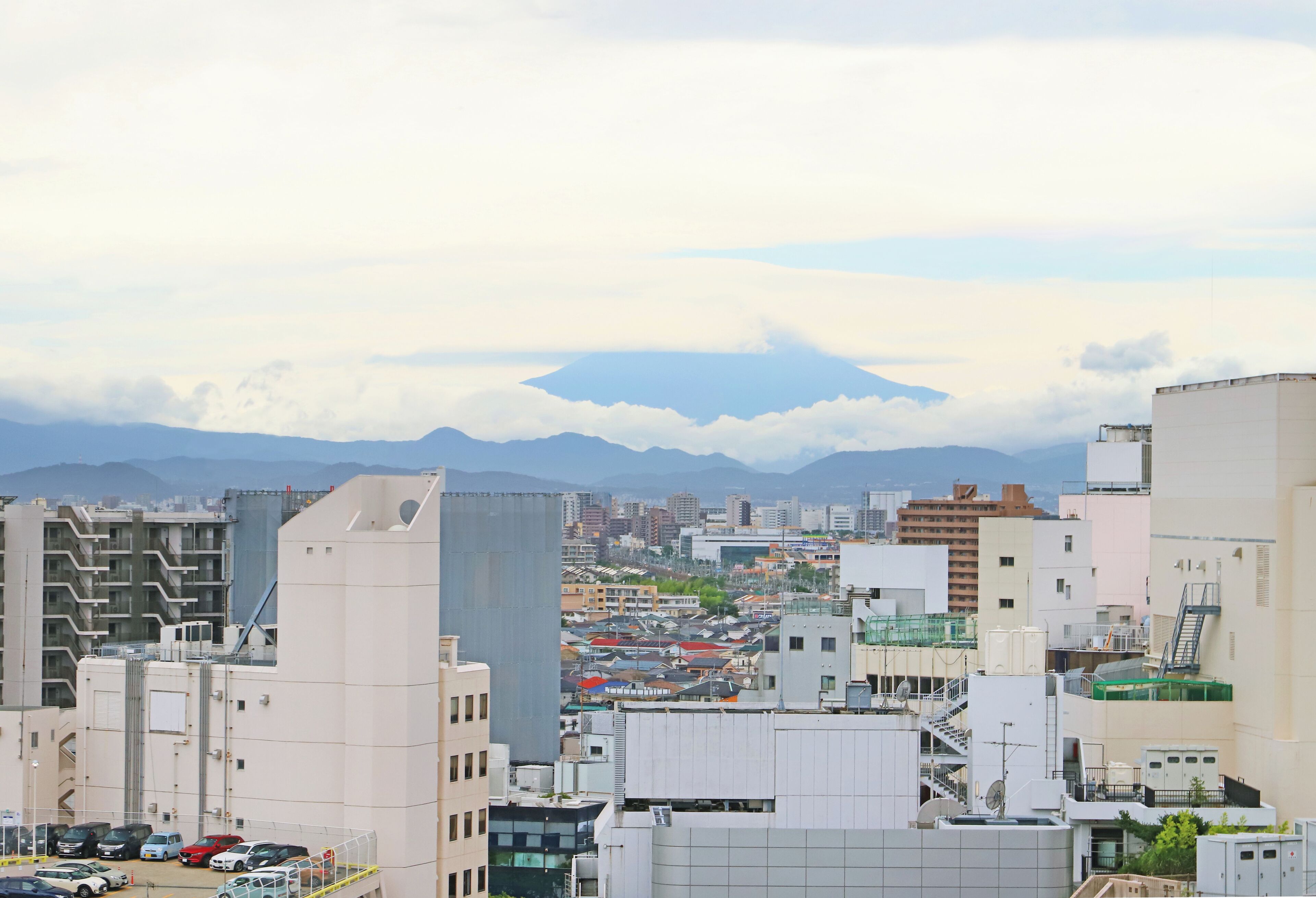 A cityscape with modern buildings, a parking lot, and distant mountains.