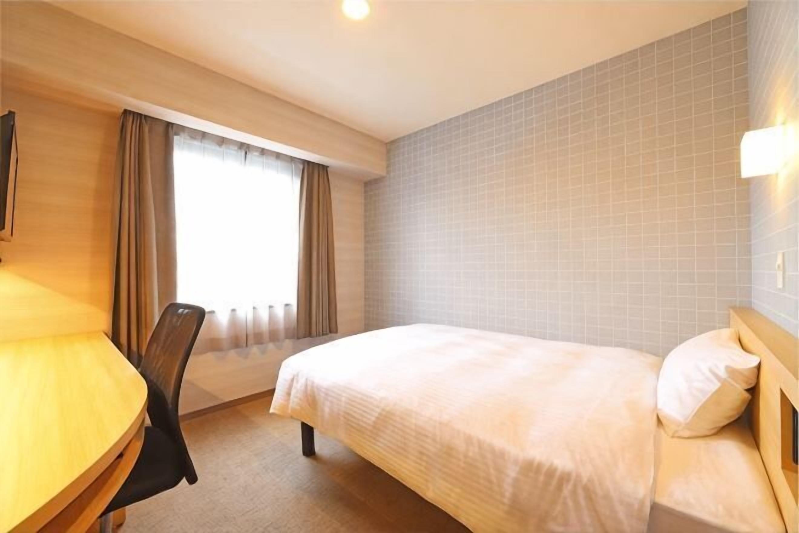 A hotel room with a bed, a desk, a chair, and a window with curtains.