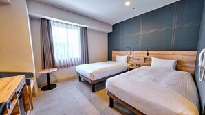 Ein Hotelzimmer mit zwei Betten, einem Schreibtisch, einem Stuhl, einem kleinen Tisch und einem Fenster mit Vorhängen.