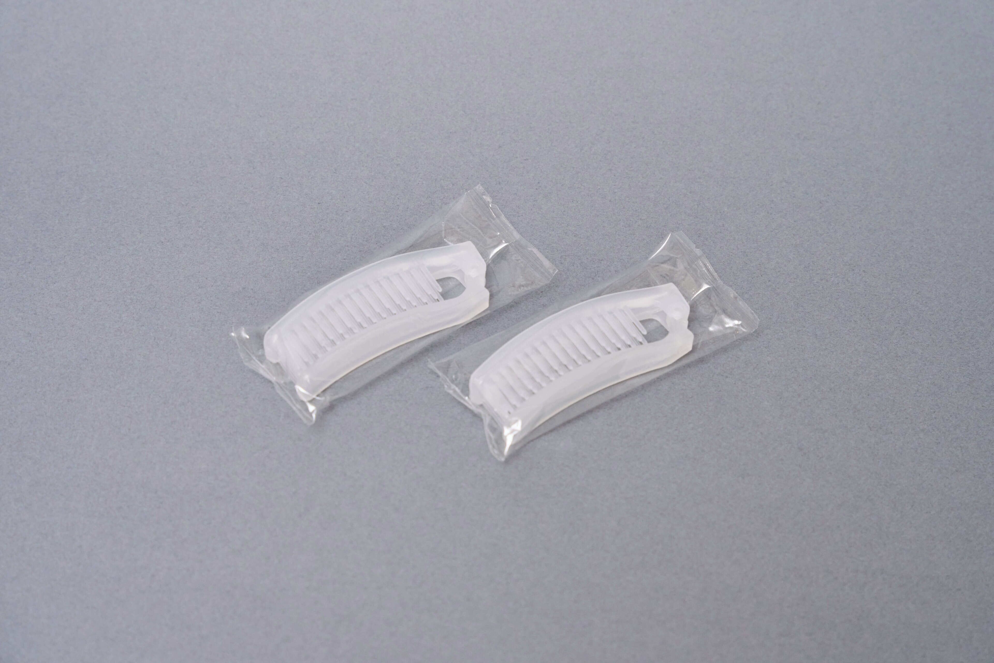 Two white objects in clear plastic packaging on a grey surface.