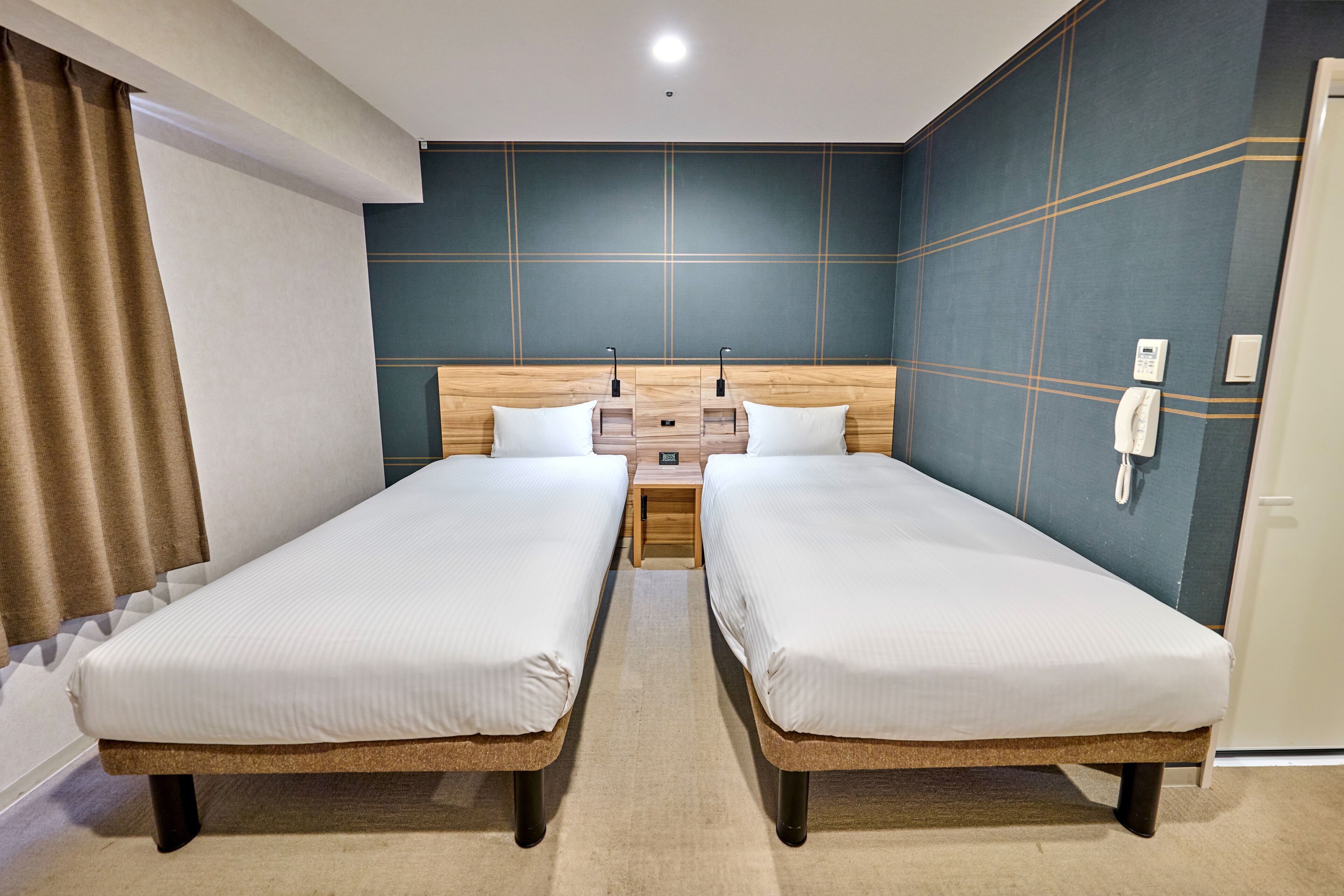 A hotel room with two single beds, a wooden headboard, a nightstand, and a telephone on the wall.