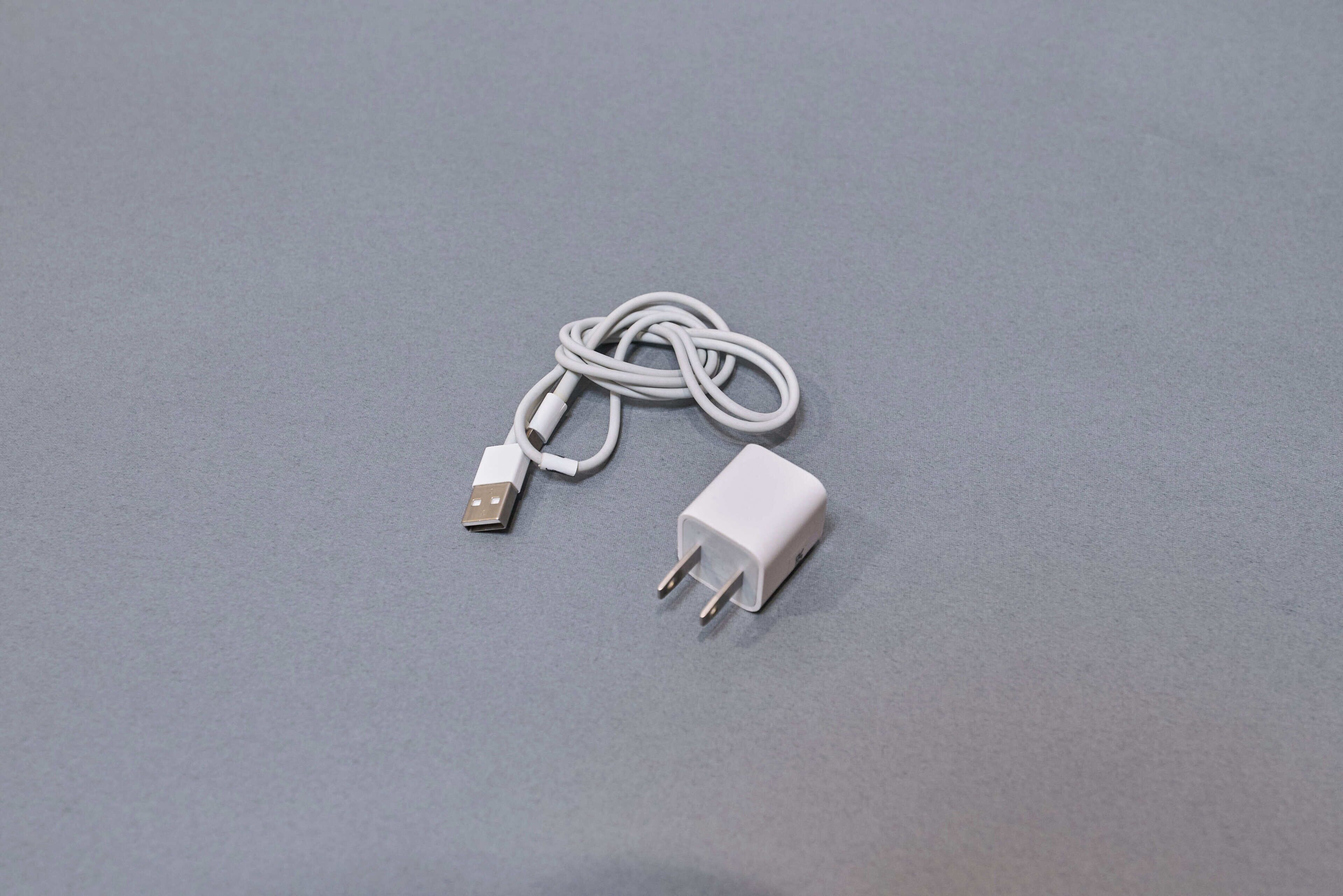A white USB cable and a white power adapter on a grey surface.