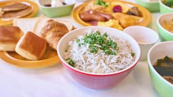 Une table où l’on peut voir différents plats, notamment un bol de riz garni d’oignons verts, des crêpes, des saucisses et des œufs brouillés.