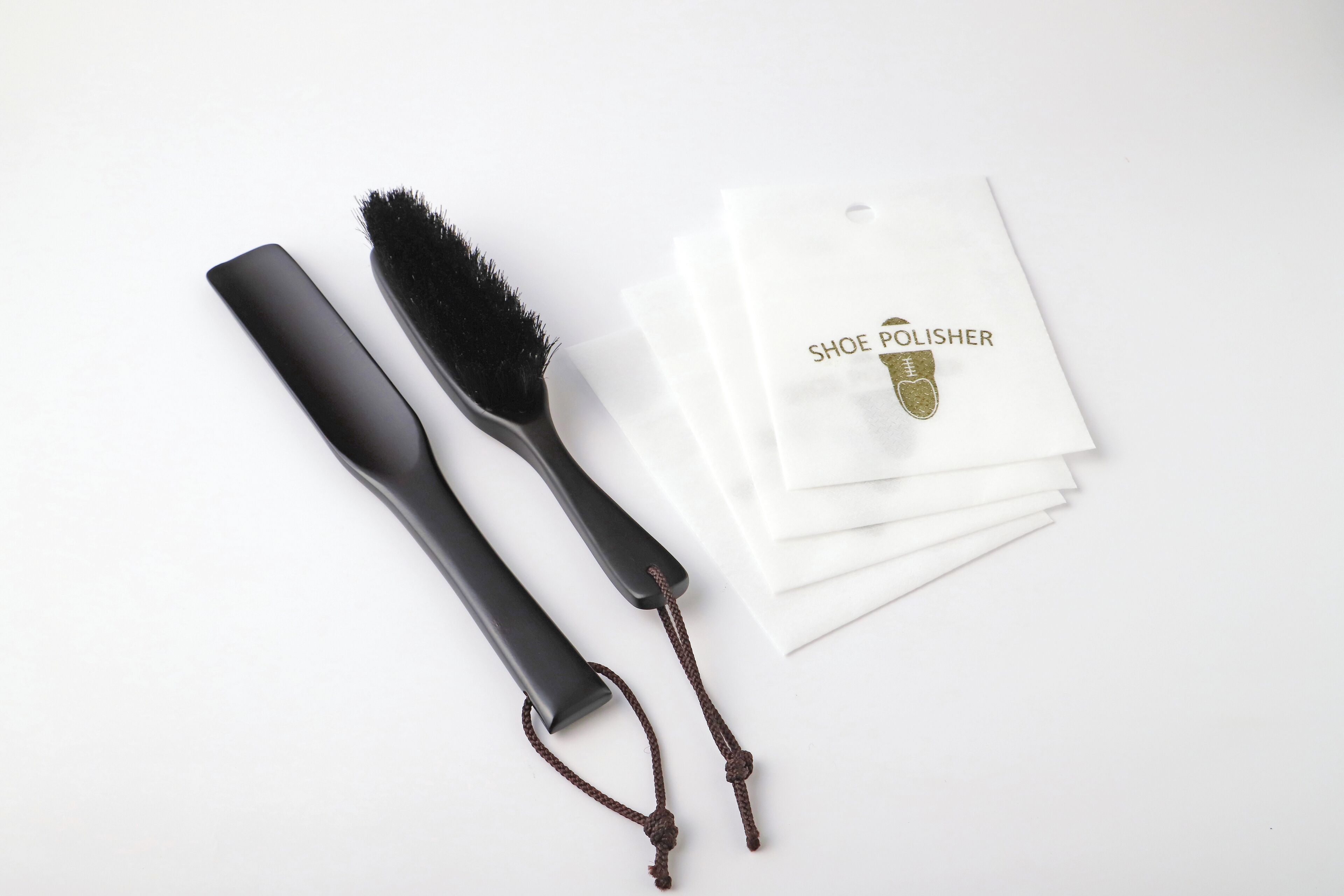 Un kit para lustrar zapatos con un mango negro, un cepillo y un paño blanco con un logo.
