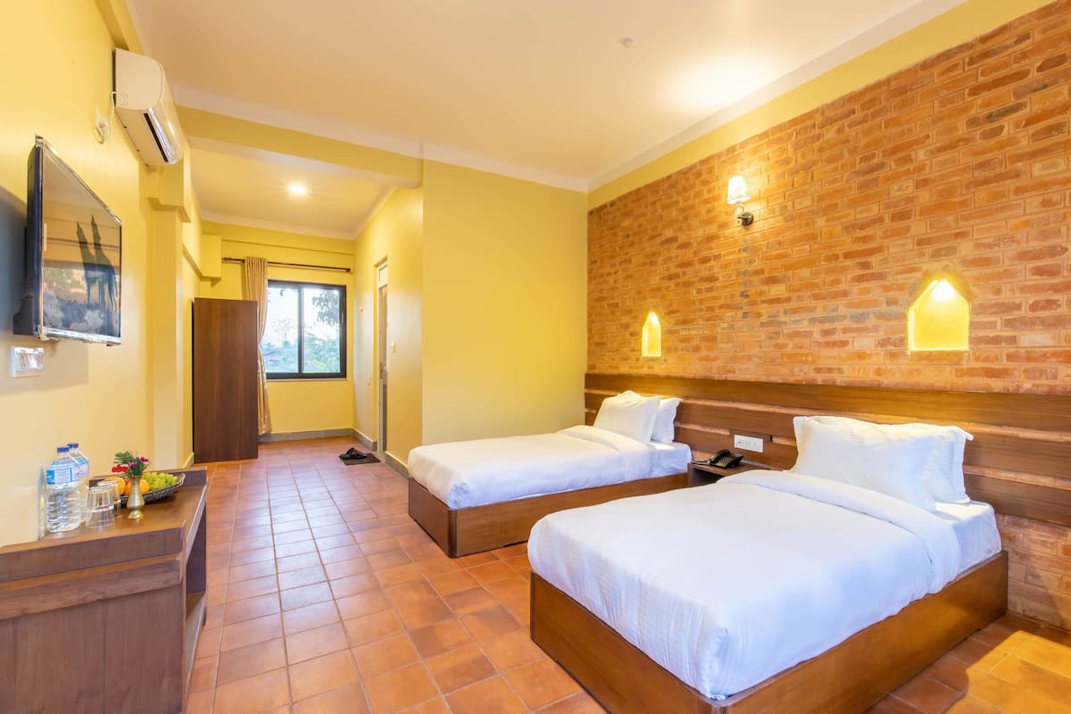 Habitación de hotel con dos camas, un cabecero de madera, una pared de acento de ladrillo, un escritorio pequeño con un espejo y una ventana con cortinas.