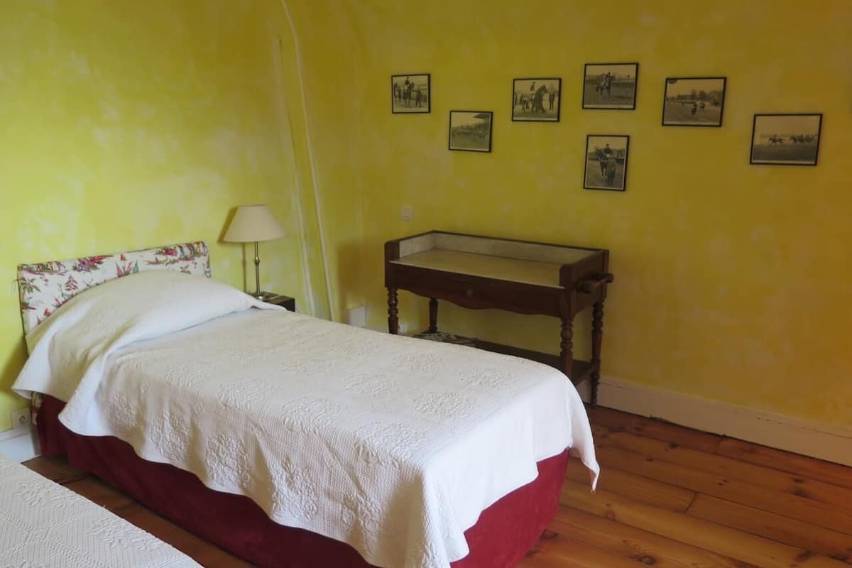 Una habitación con cama, mesita de noche, lámpara y una mesita auxiliar de madera.