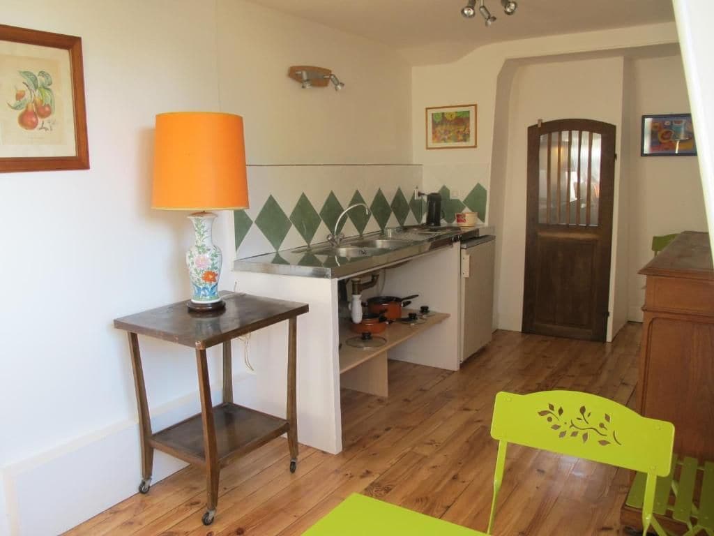 A compact kitchen with a sink, a small table with a lamp, and a chair.