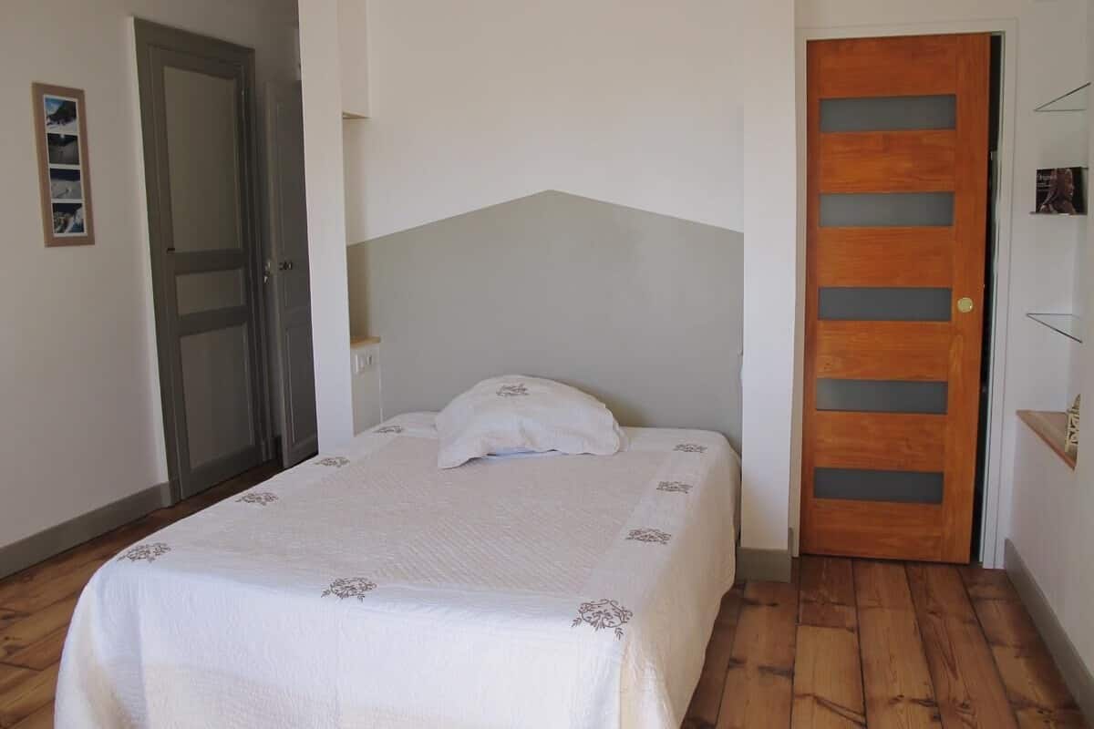 Un dormitorio con cama, puerta de madera y pared blanca.