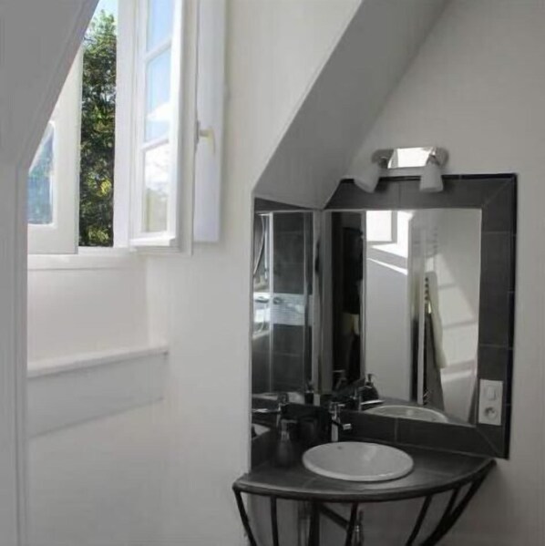 Une salle de bain moderne avec un grand miroir, un lavabo rond et une fenêtre donnant sur un paysage verdoyant.