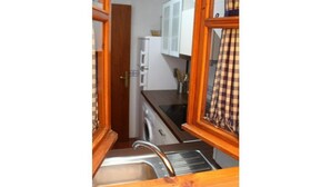 A narrow kitchen with a sink, cabinets, and a door leading to another room.