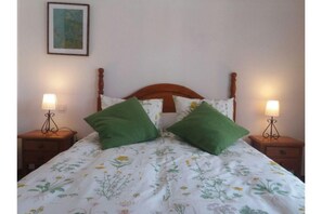 Una cama con una colcha estampada con flores, dos almohadas verdes y dos lámparas de noche sobre mesitas de madera.