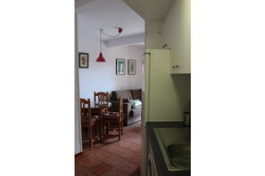 Una cocina compacta con lavamanos, una zona de comedor con sillas y una mesa, y un refrigerador pequeño.