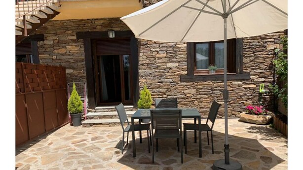 A stone patio with a table and chairs, a large umbrella, and a stone wall building in the background.