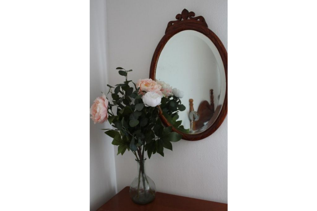 En vase med blomster på et træbord foran en væg med et spejl.