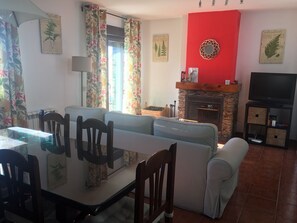 Una sala de estar con chimenea de piedra, televisor y comedor con mesa y sillas de vidrio.