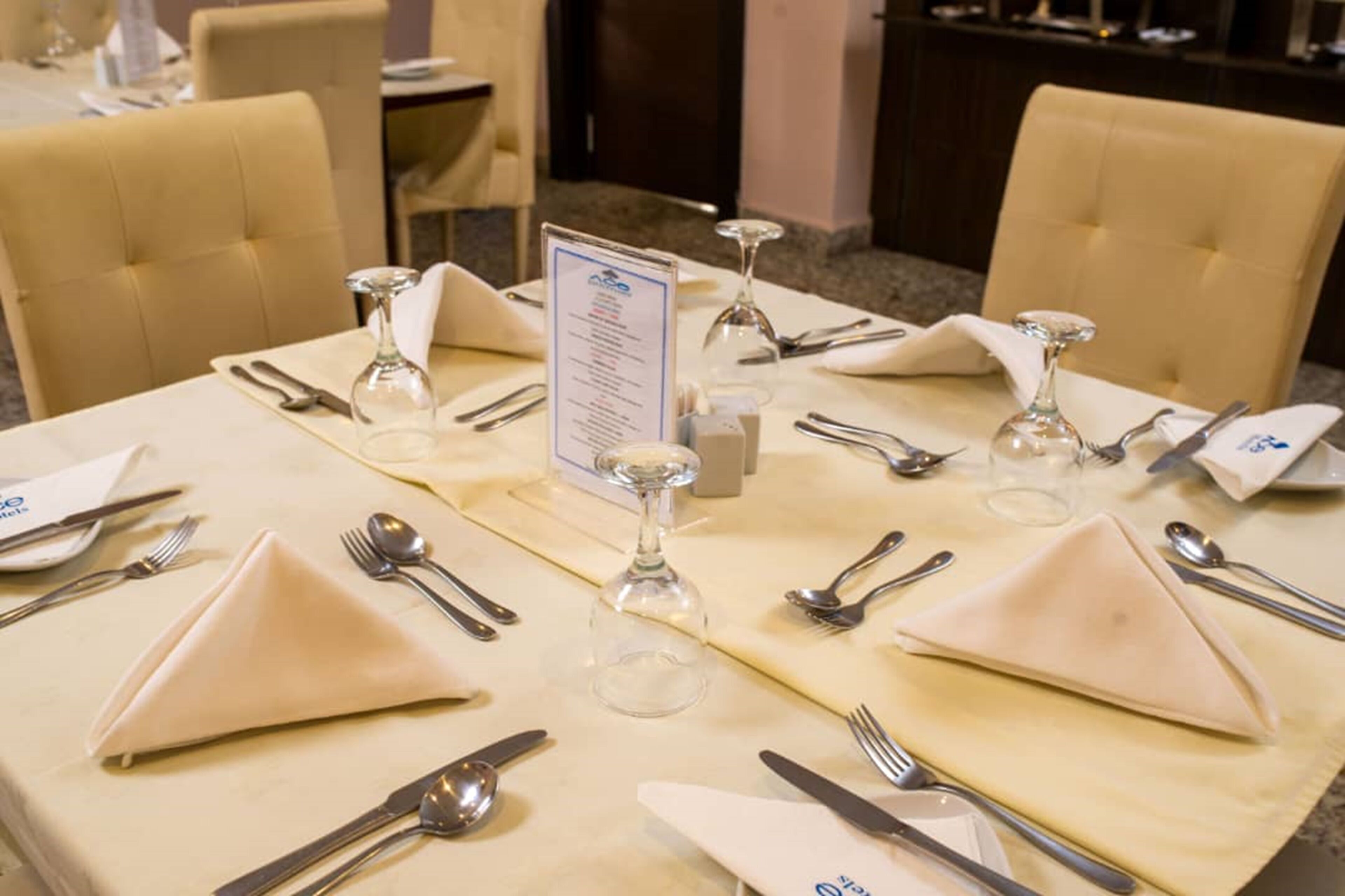 Una mesa de comedor preparada para cuatro personas, con un atril para el menú en el centro y sillas alrededor.
