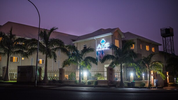 A building with a prominent logo on the facade, palm trees in the foreground, and a streetlight in the foreground. - Ace Premier Hotel (Abuja)