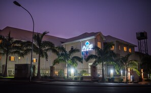 Un bâtiment dont la façade est ornée d’un logo bien visible, avec des palmiers au premier plan et un lampadaire également au premier plan.