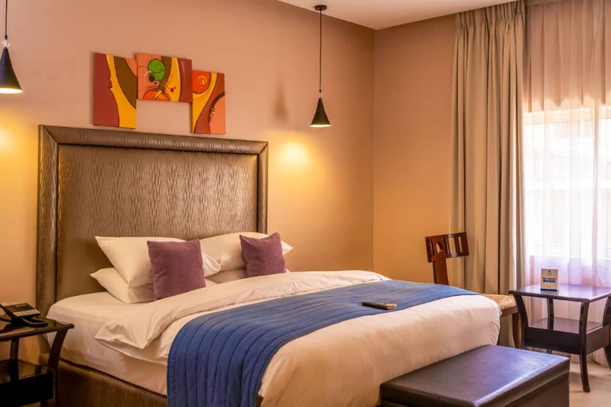 A hotel room with a large bed, a bedside table with a phone, a small table with a sign, and a chair.