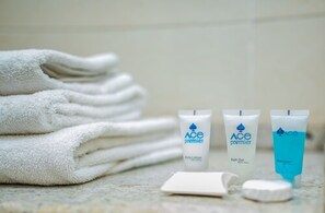 A stack of white towels, two tubes of Ace Premier body lotion, and a tube of Ace Premier bath gel on a marble surface.