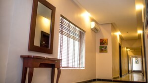 A hallway with a wooden table, a mirror, and a window with blinds. - Ace Premier Hotel (Abuja)