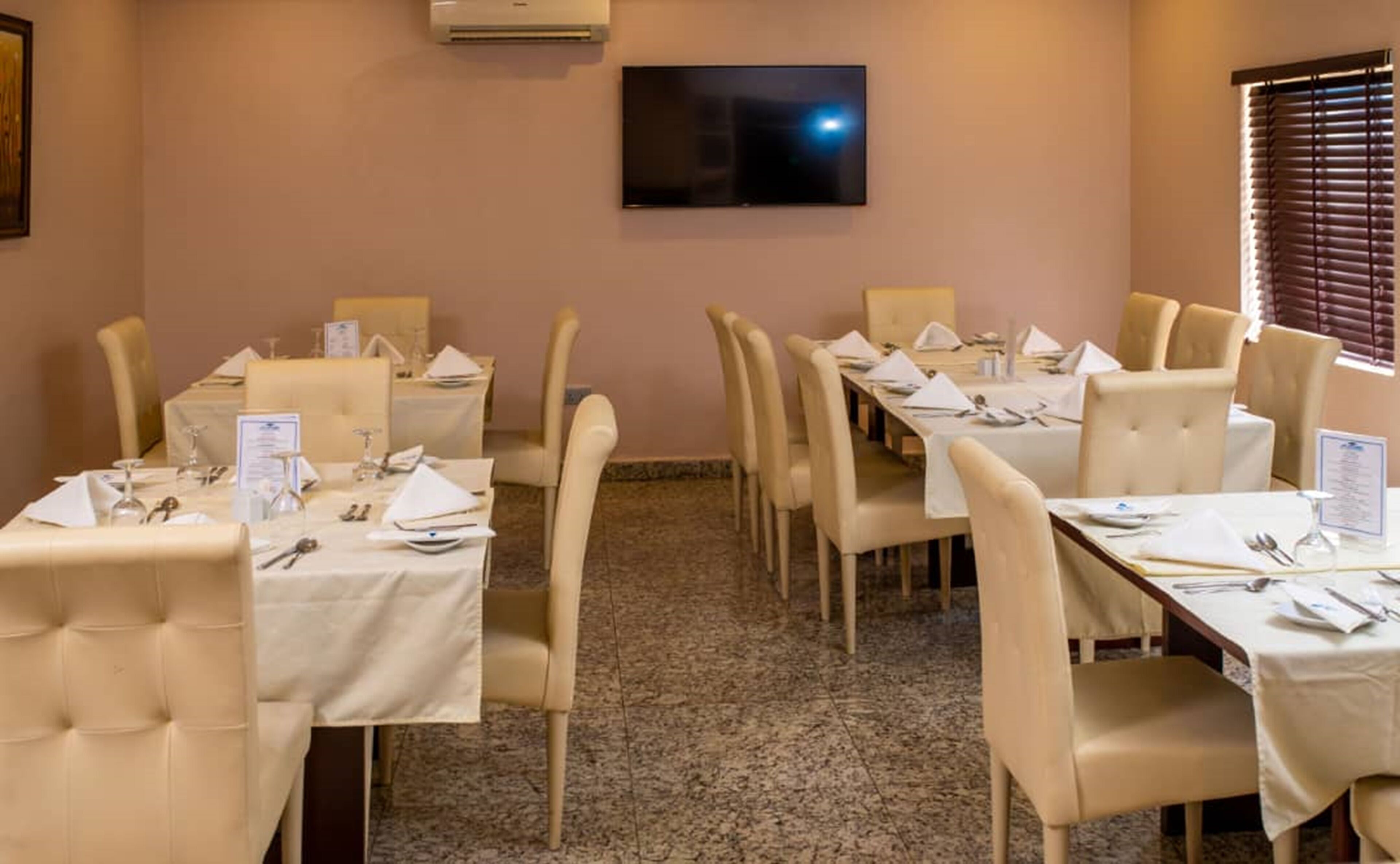 A conference room with tables set for a meeting, a flat-screen TV on the wall, and a window with blinds.