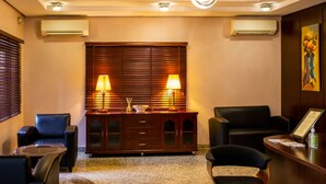 A hotel lobby with a wooden cabinet, two lamps, a painting, and a reception desk. - Ace Premier Hotel (Abuja)