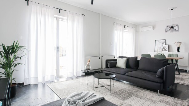 A modern living room with a black sofa, a round coffee table, and a large window with sheer curtains. - Spacious 1BD Apartment near HELEXPO Marousi (Marousi)