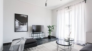 A modern living room with a sofa, a TV, a potted plant, and a glass coffee table. - Spacious 1BD Apartment near HELEXPO Marousi (Marousi)