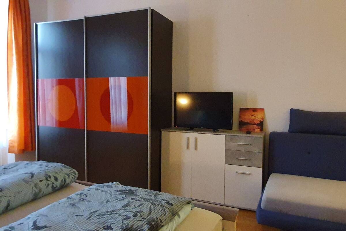 Ein Zimmer mit zwei Betten, einem Kleiderschrank, einem Fernseher und einem Bild an der Wand.