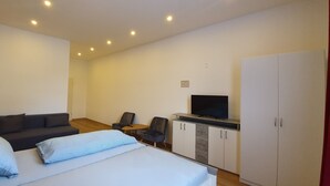 A modern hotel room with a bed, a sofa, a TV, and a wardrobe. - Trang Hotel (Rastatt)