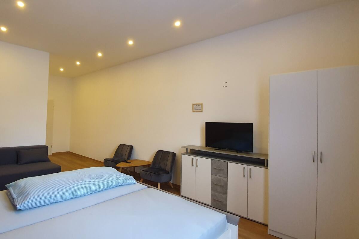 Ein modernes Hotelzimmer mit Bett, Sofa, Fernseher und Kleiderschrank.