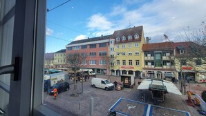 A view of a street with buildings, a white van, and a person in orange. - Trang Hotel (Rastatt)