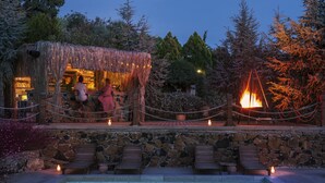 A pool area with lounge chairs, a stone wall, and a thatched-roof structure with lights. - Simurg Inn (Ayvacik)