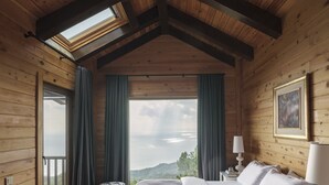 A wooden cabin bedroom with a bed, a nightstand, a lamp, and a view of the landscape. - Simurg Inn (Ayvacik)