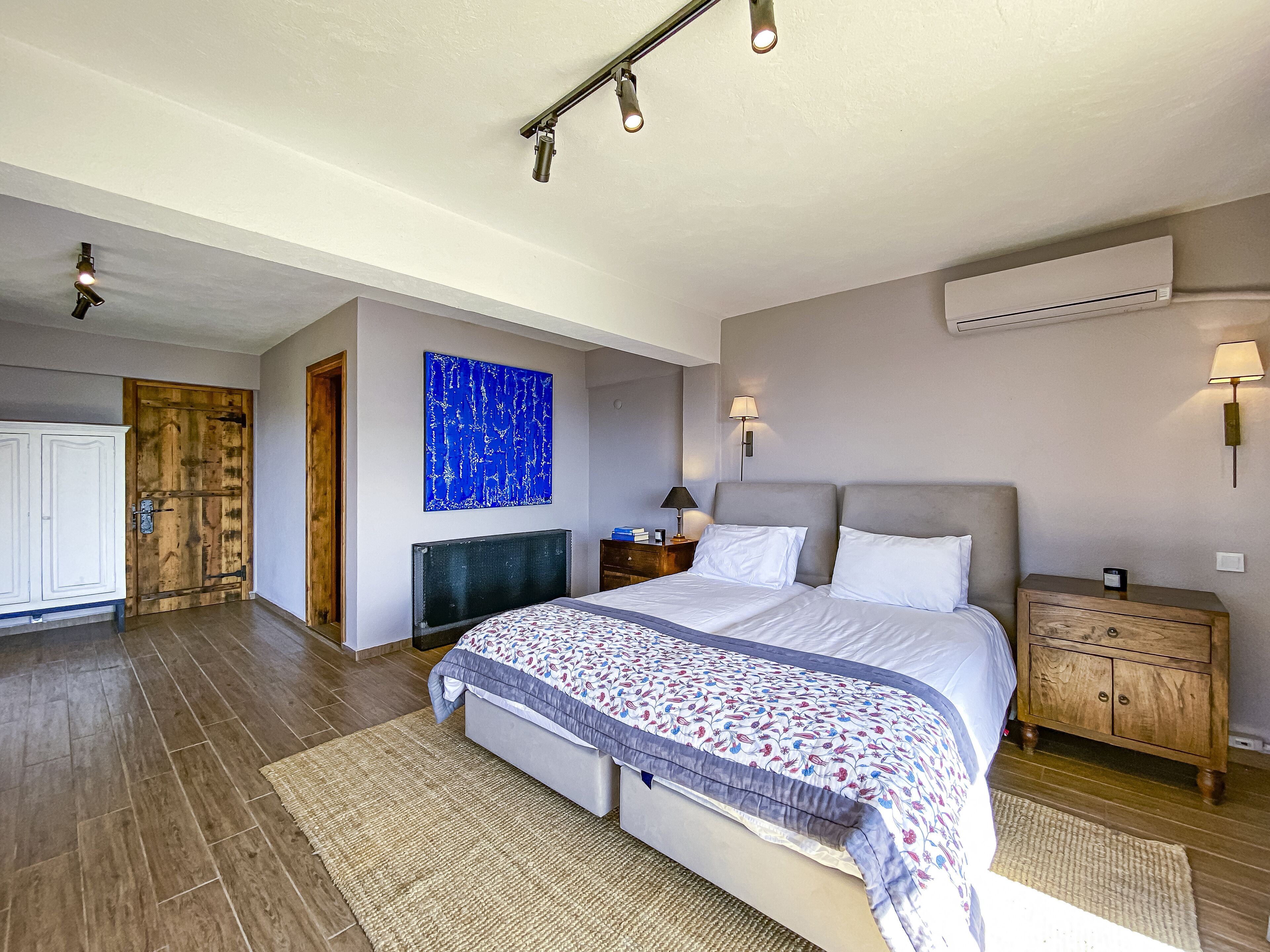 Slaapkamer met een groot bed, een nachtkastje, een wandairconditioner en een deur met een rustieke uitstraling.