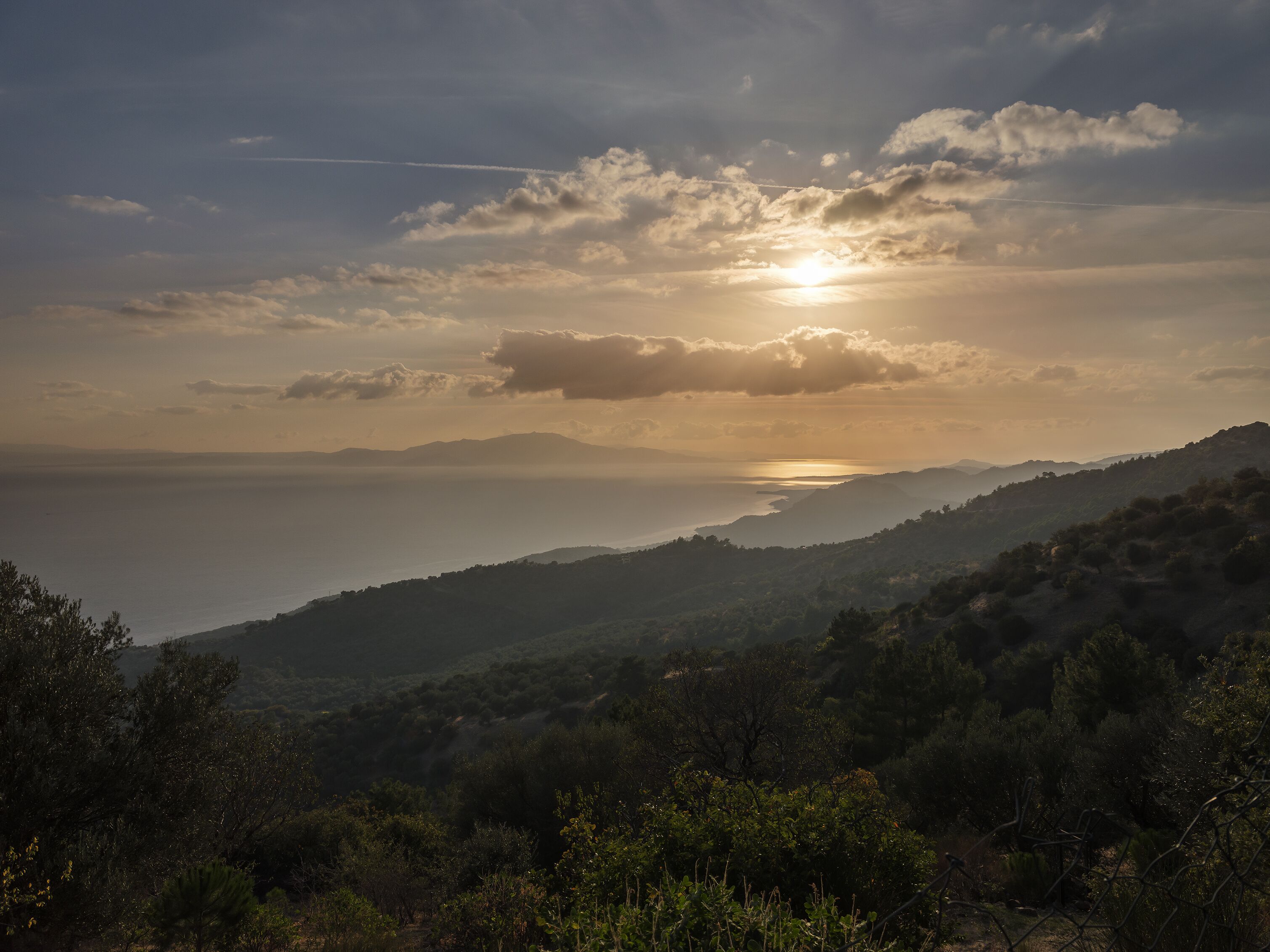 A coastal landscape with a sunset over hills and a body of water.
