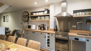 A modern kitchen with a stainless steel oven, microwave, and coffee maker on the counter. There are shelves above the counter holding plates and bowls.